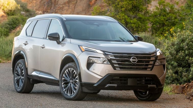 2024 m. Nissan Rogue Platinum su krūmais fone.
