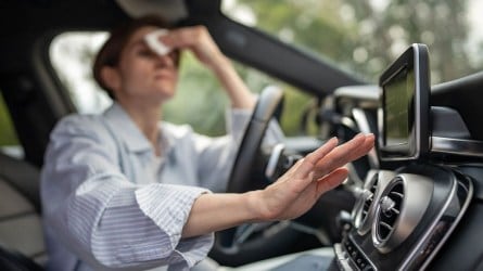 A person wiping forehead while adjusting car AC vent.