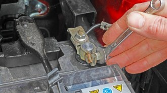 A person using a wrench to disconnect a car battery.
