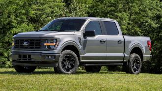 2024 Ford F-150 STX parked on grass with trees in the background.