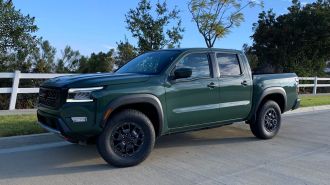 2024 Nissan Frontier in green parked next to a white fence.
