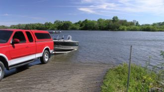 A Ford truck with an outboard boat is launched on a ramp into a lake.