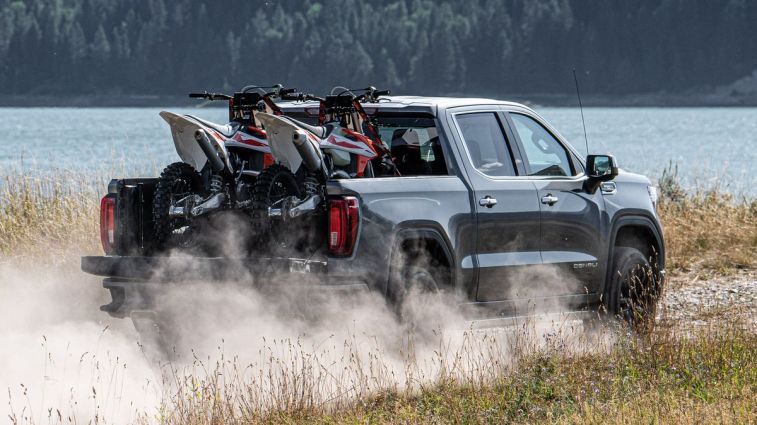 2021 GMC Sierra Denali driving on a dirt road near a lake.
