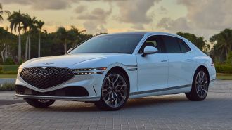 2024 Genesis G90 in white with palm trees in the background at sunset.