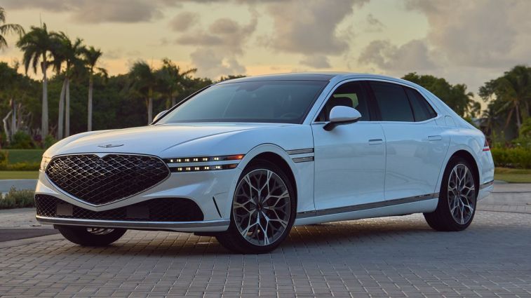 2024 جينيسيس G90 باللون الأبيض مع أشجار النخيل في الخلفية عند غروب الشمس.