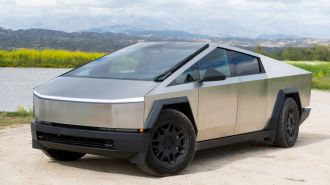 2024 Tesla Cybertruck on a dirt road with a lake and hills in the background.