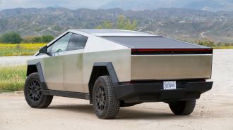 2024 Tesla Cybertruck on a dirt road with a lake and hills in the background.
