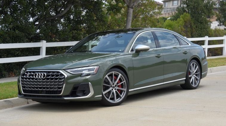 2024 Audi S8 in District Green Metallic parked near a white fence.