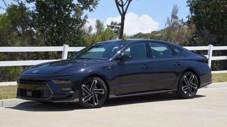 2024 Hyundai Sonata N Line in Carbon Blue with a white fence in the background.