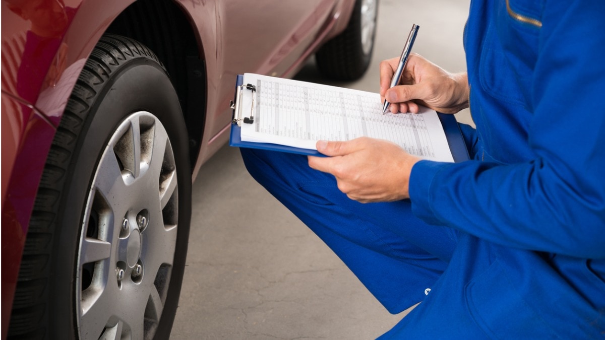 Mechanic with clipboard inspecting car