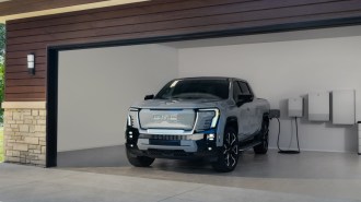 The 2025 GMC Sierra EV seen from a front quarter angle, plugged in to charge